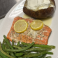 Baked salmon filet with lemon slices, green beans, and a baked potato topped with sour cream.