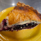 Slice of blackberry pie with a flaky golden crust and rich blackberry filling served on a yellow plate.