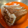 Slice of carrot cake with cream cheese frosting and chopped pecans served on an orange plate.