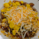 Breakfast bowl with eggs, meat, potatoes, vegetables and shredded cheese.