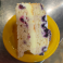 Slice of lemon berry cake with blueberries and creamy filling served on a yellow plate.