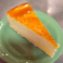 Slice of New York cheesecake with a caramelized crème brûlée topping served on a green plate.