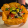Taco salad served in a crispy tortilla bowl with fresh vegetables, cheese, olives, avocado, salsa, and sour cream.